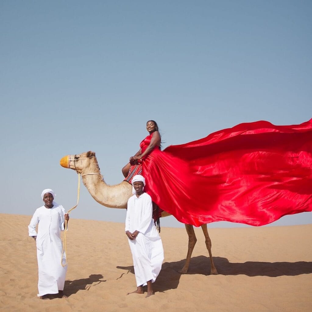 Family flying dress photoshoot in Dubai desert with red flowing dress and camel experience