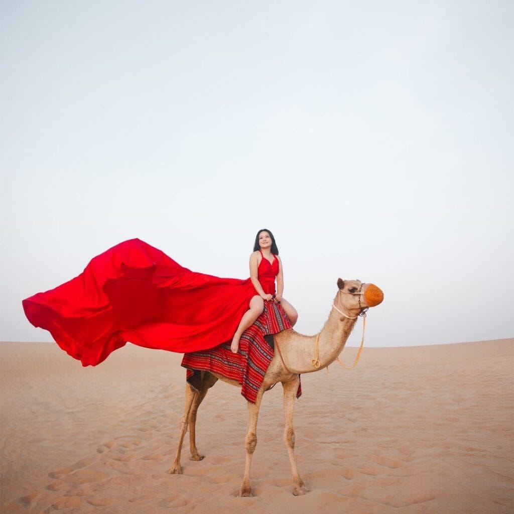 Red flying dress photoshoot in Dubai desert with camel and luxury professional photography experience